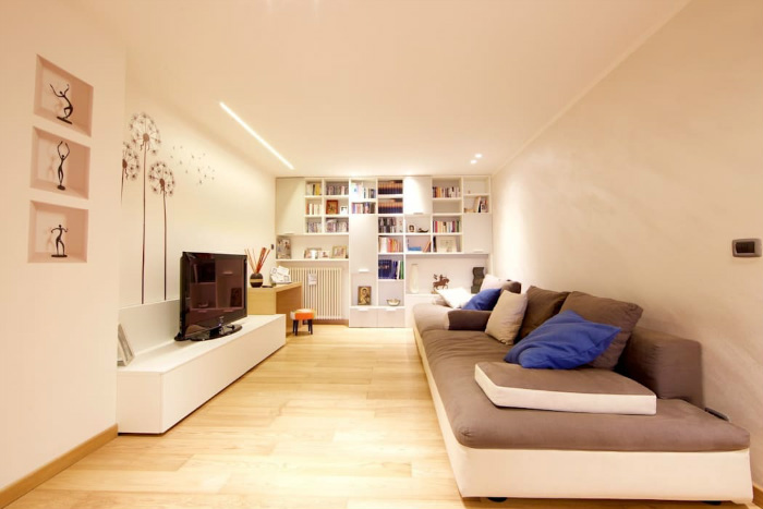 Στο απέναντι τοίχο η βιβλιοθήκη δεν πιάνει χρήσιμο χώρο, ενώ αποδίδει χώρο για βιβλία, διακοσμητικά, ενώ θα μπορούσε να έχει και κουτιά αποθήκευσης.