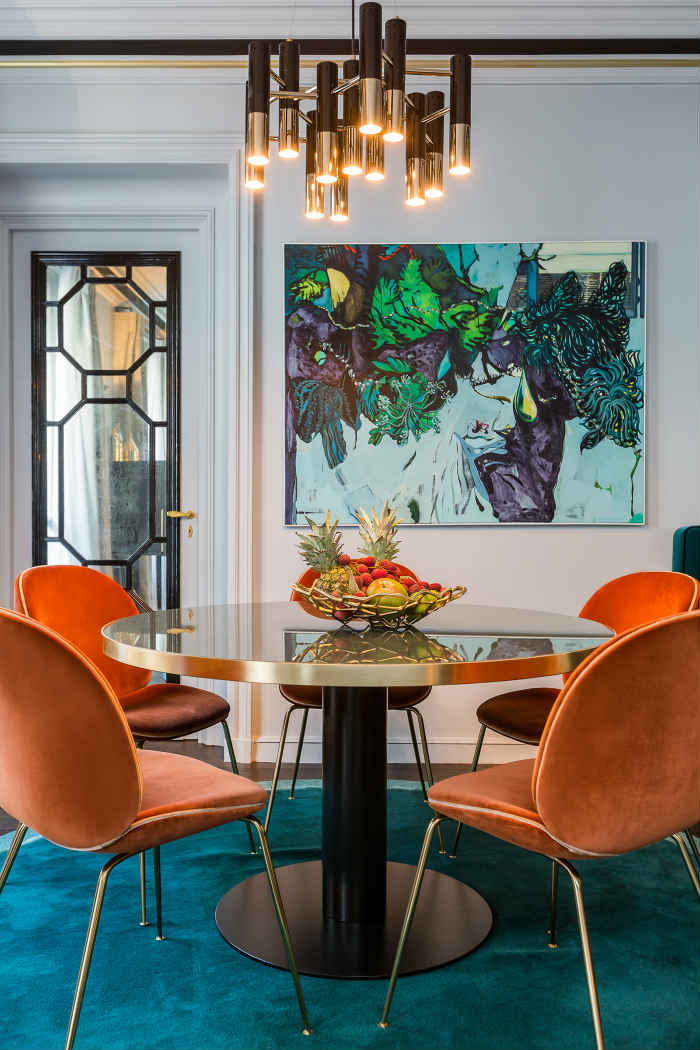 Το γαλαζοπράσινο προς πετρόλ βελούδινο χαλί τονίζει τον χώρο της τραπεζαρίας με τις beattle καρέκλες.