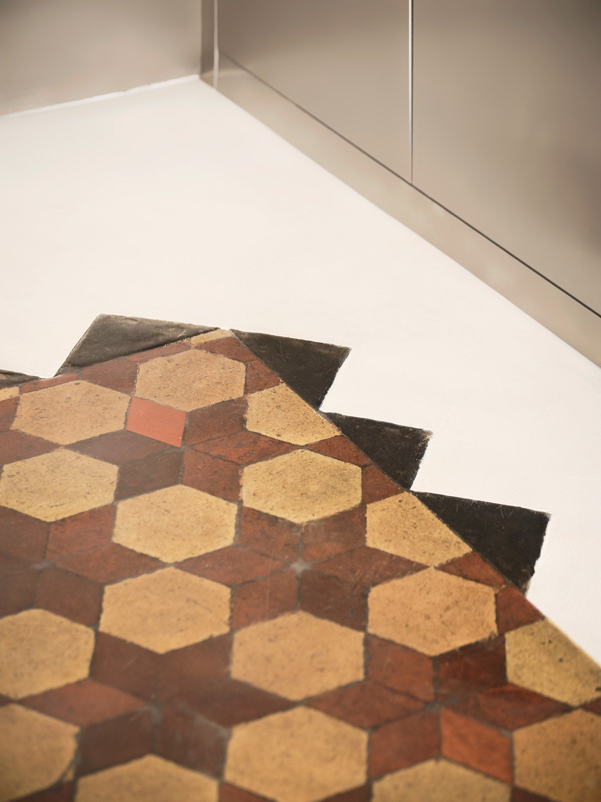 Λεπτομέρεια από εξάγωνα πλακάκια terracotta σε κόκκινο και ώχρα που σταματούν σε οδοντωτή γραμμή πάνω σε λευκό μικροτσιμέντο