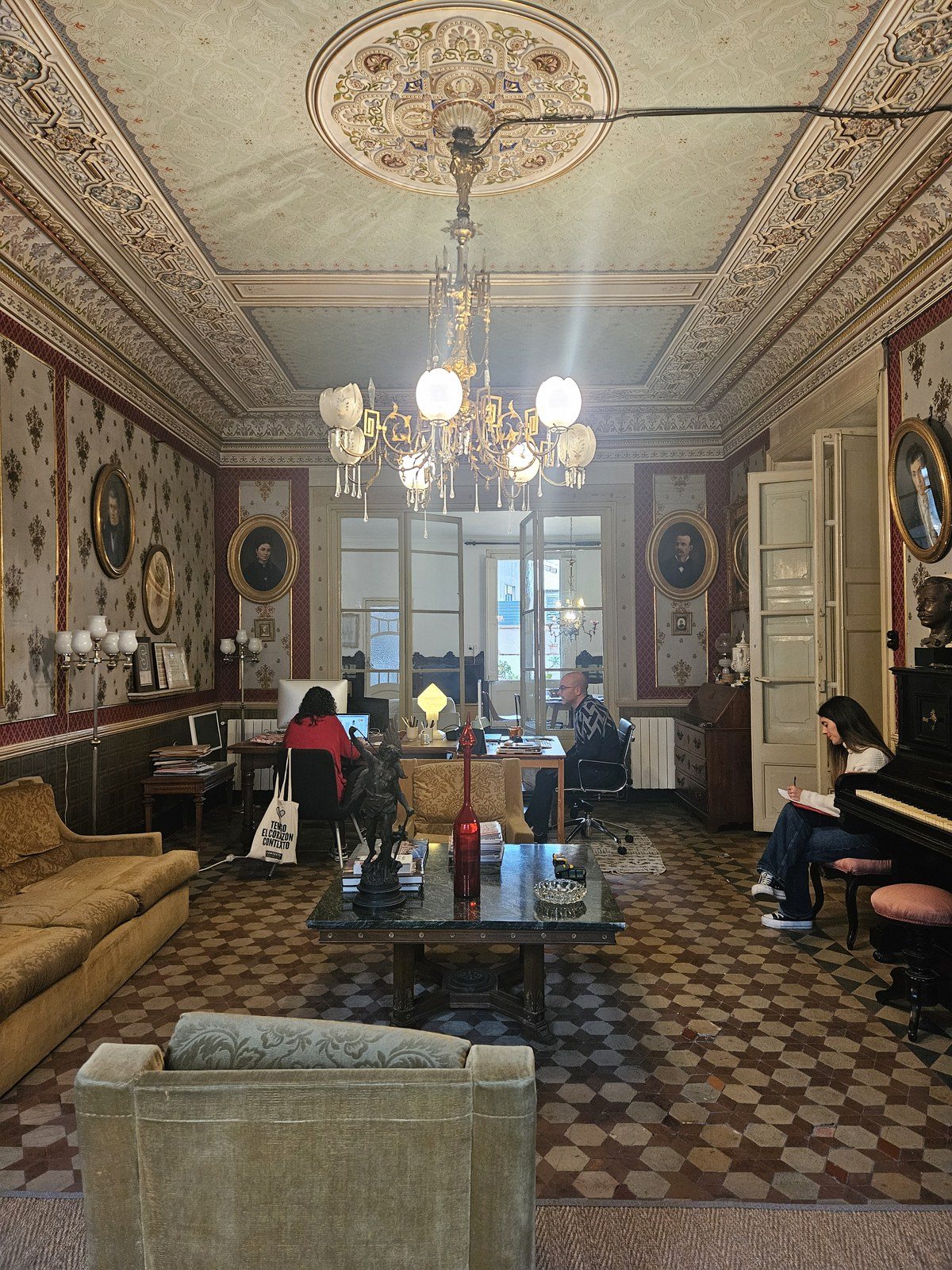 Το σαλόνι πριν την ανακαίνιση, με κρυστάλλινο πολυέλαιο, παλιούς καναπέδες, τραπεζάκι και γραφεία με υπολογιστές στο βάθος