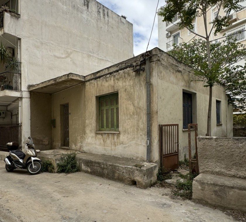 Το εγκαταλελειμμένο μονώροφο σπίτι πριν την ανακαίνιση, με φθαρμένους σοβάδες, πράσινα παντζούρια και σκουριασμένη σιδερένια πόρτα σε πάροδο