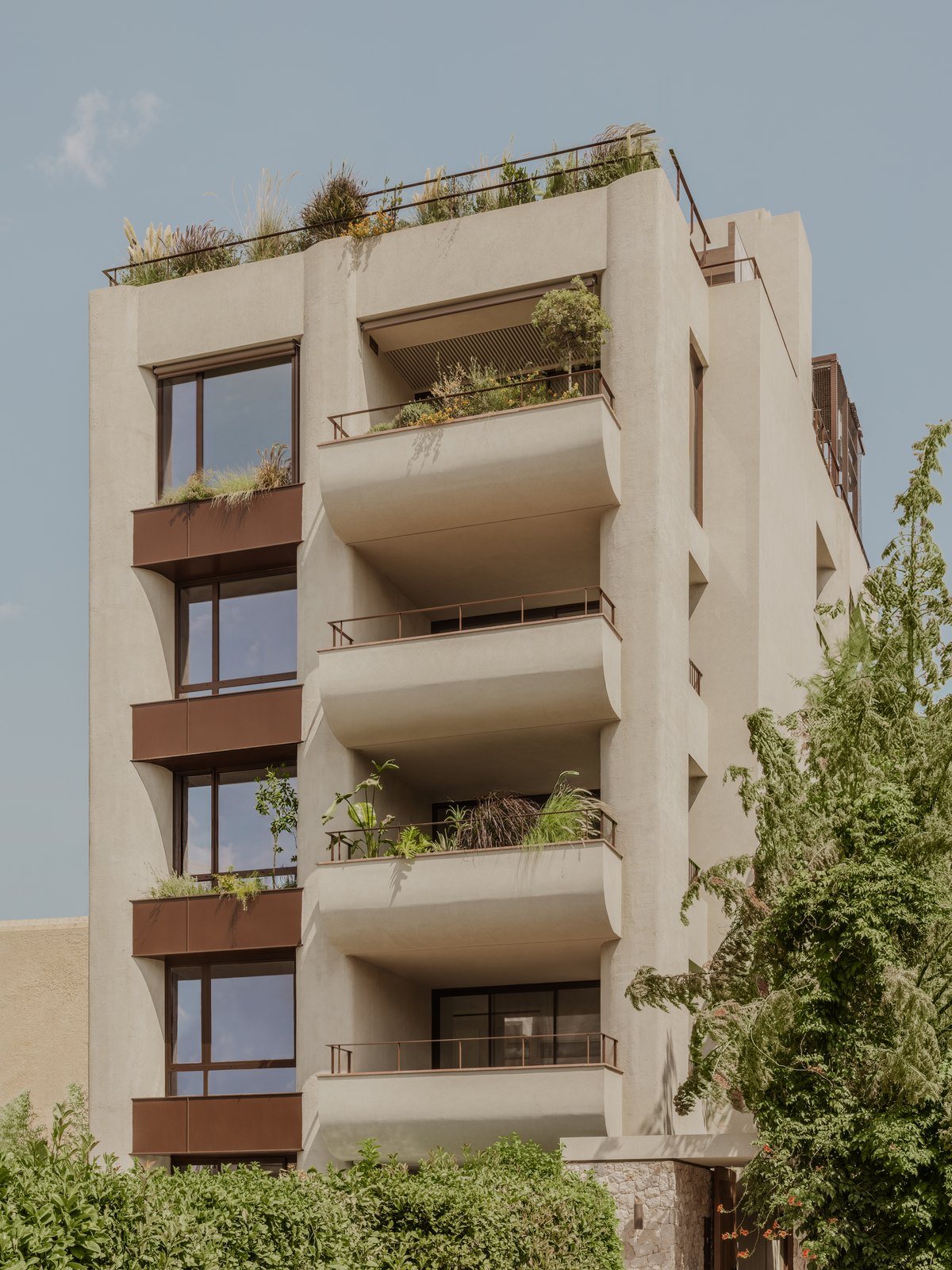 Μπεζ πολυκατοικία με καμπυλωτά μπαλκόνια, ζαρντινιέρες με φυτά και φυτεμένη ταράτσα σε δρόμο με πράσινο στον Παπάγου