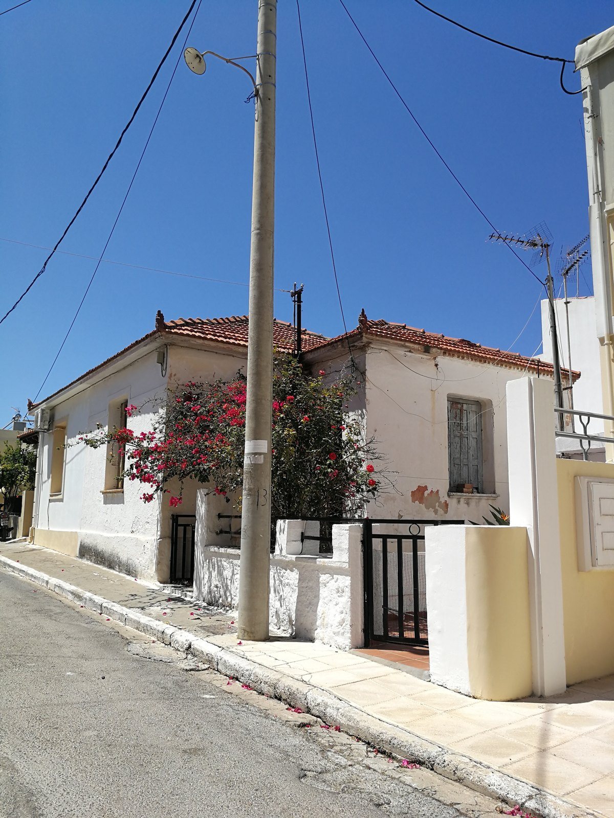 Ασβεστωμένο ισόγειο σπίτι με κεραμοσκεπή, ξύλινα παντζούρια και φούξια βουκαμβίλια, πριν την ανακαίνιση