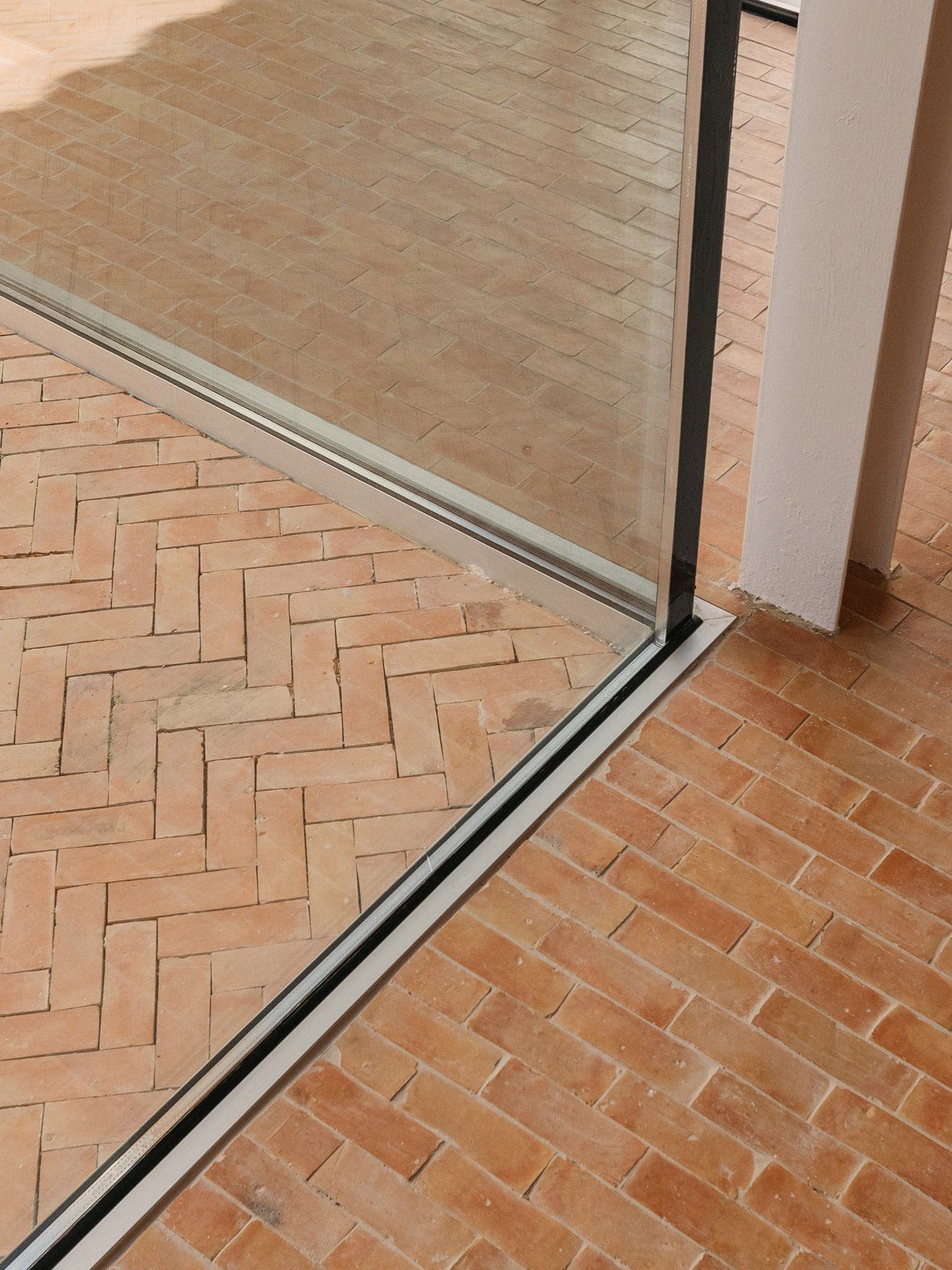 Χειροποίητα πήλινα πλακάκια σε μοτίβο ψαροκόκαλο, μέσα και έξω από μια συρόμενη τζαμαρία